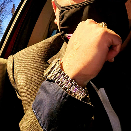 A working man wearing an elegant suit with a rolex and diamond ring and a face mask